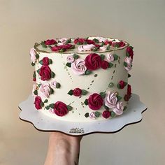 a hand holding a cake with pink and red flowers on it