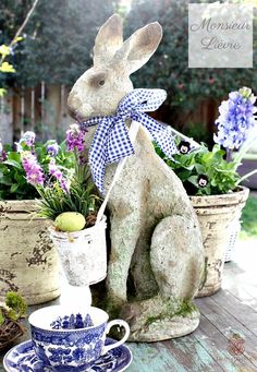 a rabbit statue sitting on top of a wooden table next to potted plants and flowers