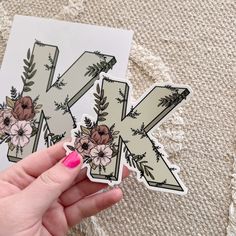 a person holding up a sticker with the letter k on it and flowers in them