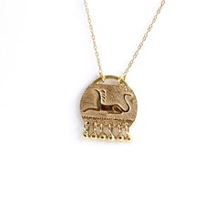 Gold hand engraved mythic animal pendant with necklace in solid gold with tiny gold dangles. A beautiful tribal necklace, fine hand work. The engrave mythic animal is a lion with bird's head. Pendant dimensions (without dangles): 10 x 12.5 mm | 0.38 x 0.49 inchMaterials: 14k solid gold (pendant & necklace).You can choose between two chain length options:1) Longer chain without clasp (to slip over your head, no fuss): 60 cm/23.622"2) Shorter chain with a gold clasp: 40 cm/15.748"Available in YELL Mythological Engraved Pendant Jewelry, Mythological Style Engraved Pendant Jewelry, Mythological Engraved Round Pendant Jewelry, Ancient Style Yellow Gold Brass Jewelry, Gold Carved Round Pendant Necklace, Carved Gold Round Pendant Jewelry, 14k Gold Engraved Amulet Charm Necklace, Engraved 14k Gold Amulet Charm Necklace, Gold Engraved Mythological Necklaces