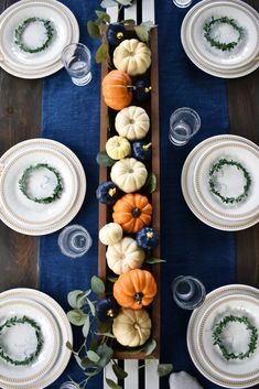 the table is set with pumpkins and greenery