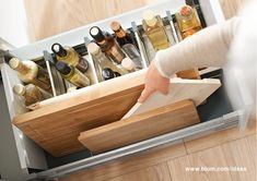 a person holding a knife and cutting board in an open drawer with bottles on it