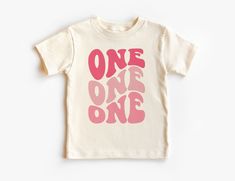 Retro First Birthday Toddler Shirt - Girls Pink Groovy 1ST Birthday Kid's Tee - One Birthday Party Theme - Boho Natural Toddler & Youth Tee If you love super soft, lightweight, extremely comfy shirts and baby bodysuits then you will absolutely love our unisex kids shirts and baby bodysuits! These shirts are hand printed with a professional garment printer for a soft, durable, long lasting, printed graphic using high quality water based inks. * The printed design is very soft to the touch due to Pink Birthday Top With Text Print, Pink Birthday Tops With Text Print, Pink Tops With Text Print For Birthday, Pink Birthday Shirt For Summer, Pink Summer Birthday Shirt, Pink Custom Print Birthday Top, Pink Custom Print Top For Birthday, Pink Graphic Print Top For Birthday, Pink Number Print T-shirt For Birthday