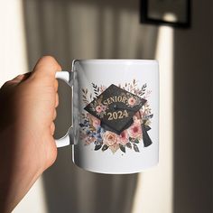 a person holding a white coffee mug in their left hand with the words senior 2020 printed on it