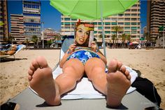 a woman laying on top of a beach under an umbrella