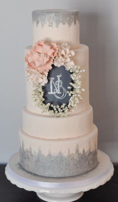 a three tiered wedding cake with flowers on the side and a monogrammed topper