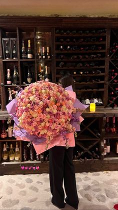 a person holding a bouquet of flowers in front of a wine rack filled with bottles