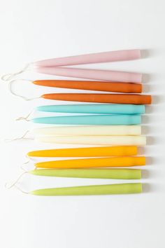 six different colored candles are lined up on a white surface with string attached to them