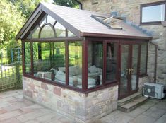 a patio area with couches, chairs and a glass enclosed room in front of a stone building