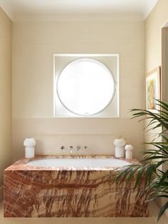 a bath tub sitting under a round window next to a potted palm tree in a bathroom