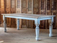 an old white table sitting on top of a wooden floor next to shuttered doors