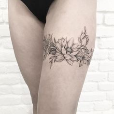 a black and white photo of a woman's thigh with flowers tattooed on it