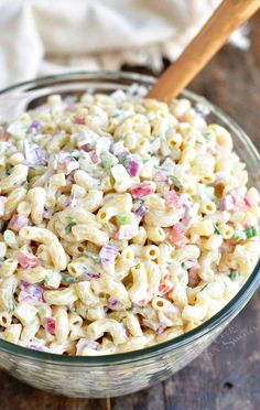 a glass bowl filled with macaroni salad on top of a wooden table next to a white towel