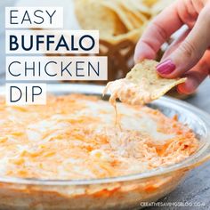 a hand dipping a tortilla chip into a cheesy buffalo chicken dip