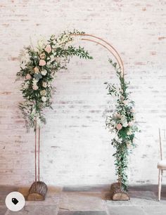 an arch decorated with flowers and greenery stands in front of a white brick wall