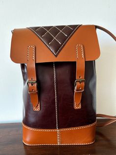 This is an unique item. Beautiful hand sewn leather backpack. The colour of the main bag is dark - a bit marbled - brown. The bottom, flap and straps are the colour cognac. The bottom, flap and straps are natural veg tan leather. The body is softer and a little thinner leather. Buckle closure.  The backpack has one inside pocket behind the quilted piece at the back. Width: 23 cm / 9 in Height: 35 cm / 13.5 in The bag will be sent as standard air mail with Danish courier PostNord with no tracking Daily Use Brown Backpack With Leather Trim, Brown Flap Satchel For Everyday, Cognac Leather Satchel Backpack With Leather Handles, Brown Everyday Flap Satchel, Everyday Brown Flap Satchel, Cognac Leather Backpack With Leather Lining, Cognac Leather Satchel Backpack With Leather Lining, Cognac Leather Satchel Backpack With Lining, Leather Backpack Shoulder Bag With Leather Trim