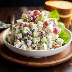 a white bowl filled with salad on top of a wooden table next to some bread