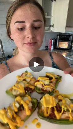 a woman is holding a plate with stuffed peppers on it and looking at the camera