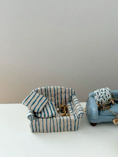 two miniature blue chairs sitting next to each other on a white counter top, one with a pillow and the other with a purse