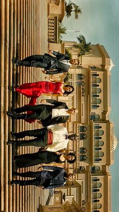 four people standing in front of a tall building with a clock tower behind them and palm trees on the other side