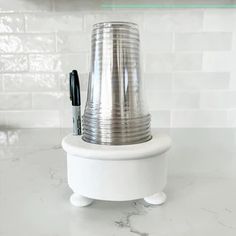 a white counter top with a silver vase on it and a pen in the holder