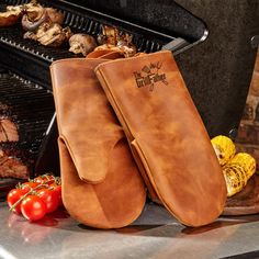 two oven mitts sitting on top of a grill next to some vegetables and meat