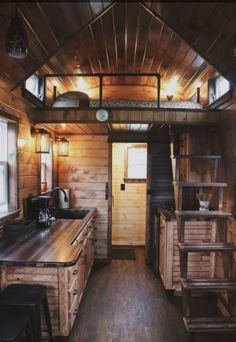 the inside of a tiny cabin with wood floors and walls, lights on above the kitchen counter