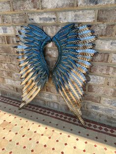 a metal sculpture on the side of a brick wall with blue and gold wings hanging from it's sides