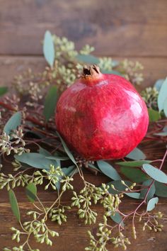 the pomegranate is surrounded by greenery and leaves on a wooden surface