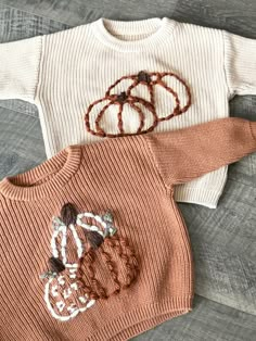 two knitted sweaters sitting on top of a wooden floor next to each other