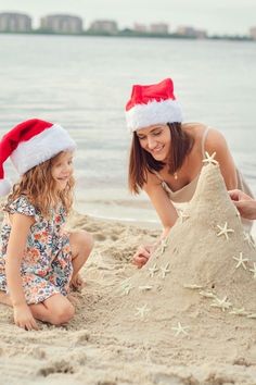 a mother and daughter building a sand castle on the beach with santa hats on their heads