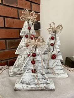 two wooden christmas trees with bows and berries on them sitting on a table next to a brick wall