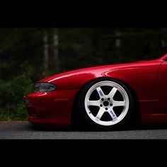 a red sports car is parked on the side of the road in front of some trees