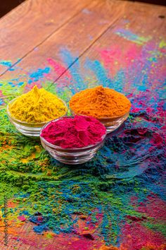 three bowls filled with colored powder on top of a wooden table