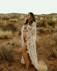 a pregnant woman standing in the desert wearing a white lace dress with sheer sleeves and open crotchers