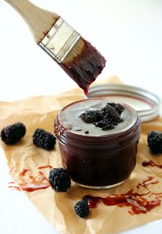 a paintbrush with some food in it and blackberries on the ground next to it