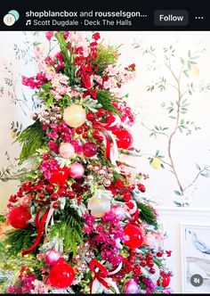 a christmas tree decorated with red, white and pink ornaments is shown in front of a wall