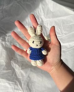 a small crocheted bunny in a blue shirt is held up by someone's hand