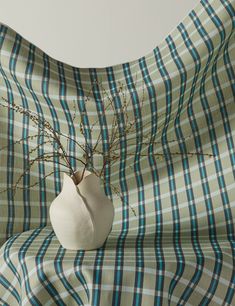 a white vase with branches in it sitting on a plaid blanket