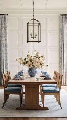 a dining room table with blue chairs and white flowers in vases on the table