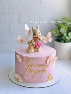 a pink cake decorated with gold butterflies and a bunny on top