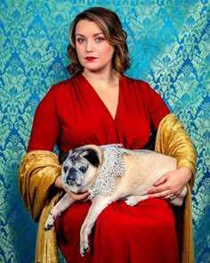 a woman in a red dress is holding a pug on her lap and posing for the camera