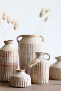 three white vases sitting next to each other on top of a wooden table with dry grass in them