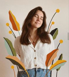 a woman with her eyes closed standing in front of a floral wallpaper design that has leaves and flowers on it