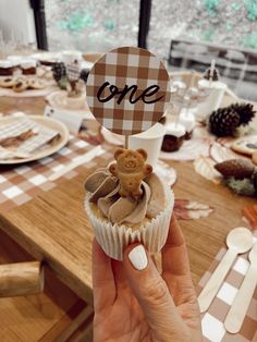 a person holding up a cupcake with a teddy bear on top that says one