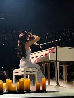 a woman sitting at a piano on stage with candles around her and an instrument in front of her