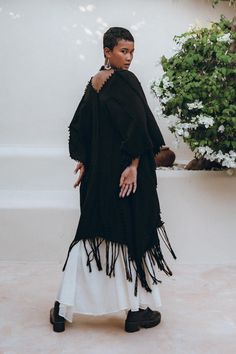 This black poncho cape is unique as each knot is tied by hand connecting the lines of this garment. This boho poncho for women is really a masterpiece. Our poncho is made of homespun cotton, which is also made by hands with the help of wooden weaving loom machine. Our brand focus on manual production, thereby giving each product a unique vibration and shape and when each knot is made with love, you can feel it while wearing it. This authentic production also supports traditional crafts and provi Black Bohemian Poncho Shawl, Black Long Sleeve Poncho For Beach, Black Long Sleeve Beach Poncho, Black Bohemian Cape For Festivals, Bohemian Black Cape For Festival, Bohemian Black Poncho For Fall, Black Oversized Bohemian Cape, Bohemian Black Poncho With Tassels, Black Shawl Poncho For The Beach