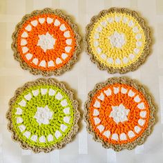 four crocheted coasters on a table with white and orange circles in the middle