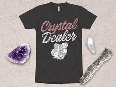 Mystical "Crystal Dealer" Graphic Design with Crystal Cluster. As a metaphysical company, we design shirts and sweatshirts that express magical and spiritual ideas. This t shirt is perfect for the divination student, tarot card reader, or witch. Makes a great gift for your favorite psychics, mediums, spiritualists, tarot card readers, crystal collector, and new age shoppers. Available on a t-shirt, sweatshirt, hoodie, racerback tank, even a children's shirt! ☽ *  UNISEX SHIRT  * ☾ T-Shirt is lightweight and soft to the touch, with the perfect amount of stretch. Super comfortable with the unisex cut flattering on both men and women. Best-selling favorite among many customers! * 100% combed and ring-spun cotton (heather colors contain polyester) * Fabric weight: 4.2 oz (142 g/m^2) * Shoulder Crystal Shirt, Spiritual Ideas, Occult Clothing, Tarot Card Readers, Design Shirts, Classic Wardrobe Staples, Card Reader, Crystal Cluster, T Shirt Women