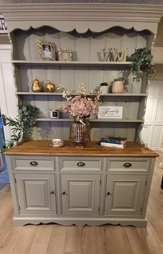 an old dresser with flowers on top and some bookshelves in the back ground